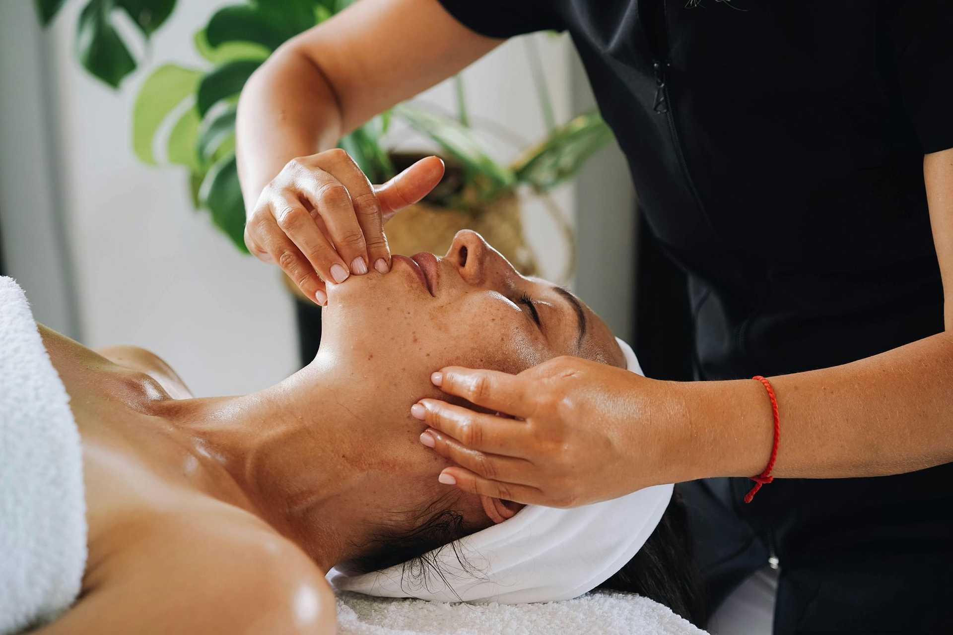 Person receiving a facial massage at a spa, hands gently on the face under serene lighting.